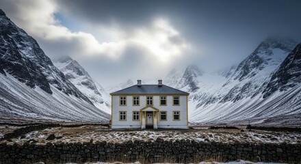 Isolated white house nestled between dramatic snow covered mountains under a cloudy sky