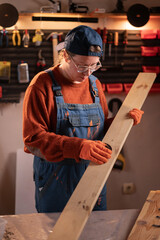 professional carpenter works with wood using carpentry tools in her garage. She holds a laptop and sands a board with sandpaper. Concept of profession, art, and hobby.