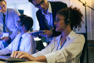 Professional team of diverse agents providing customer support in a modern tech office. Specialists wearing headsets monitor digital data while a manager offers technical guidance and assistance