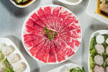 A white plate with thinly sliced raw beef arranged in a fan shape, garnished with fresh parsley on...