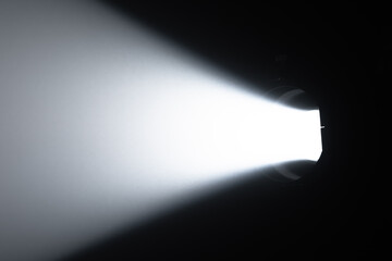 A powerful, focused beam of white light emanating from a spotlight in a dark room creates striking contrast and atmosphere. Lighting equipment backstage.