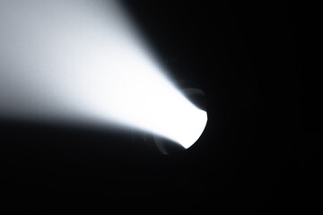 A powerful, focused beam of white light emanating from a spotlight in a dark room creates striking contrast and atmosphere. Lighting equipment backstage.
