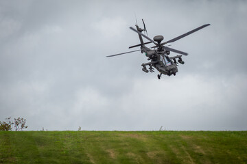 Apache attack helicopter or AH64 can be seen flying low over a grass hill on Salisbury plain during a dark cloudy day