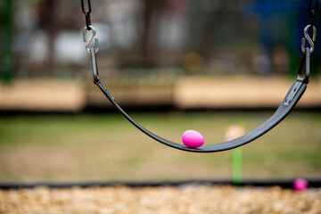 Colorful pink plastic Easter eggs placed on empty playground swing seat with wood chip mulch surface below. Perfect for illustrating spring community events, Easter egg hunts &children's activities
