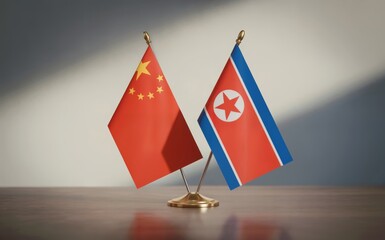 Studio image of China and North Korea flags standing together on a polished wooden desk against a gray wall with diagonal shadow Bright lighting emphasizes international relations diplomacy and partne