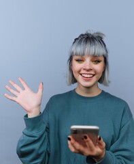Young woman with gray hair waving and holding a smartphone.