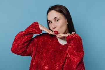 Woman in red sweater posing playfully against blue background.