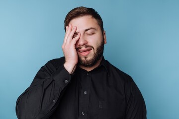 Obraz premium Man in black shirt with hand on face against blue background.