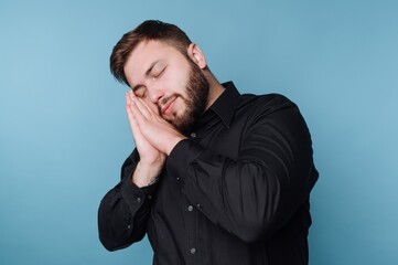 Man in black shirt mimicking sleep against blue background.