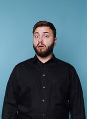 Fototapeta premium A surprised man with a beard and black shirt against a blue background.