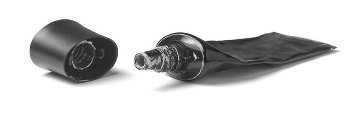 empty squeezed black plastic cosmetic tube and detached cap isolated white background, glossy finish container with matte lid and dented surface texture, side closeup view