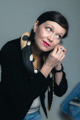 Portrait of attractive young business woman at home with collected dark hair placing her earrings and wearing black jacket.