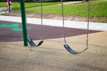 Empty playground swings hang motionless in a public park, capturing a quiet daytime moment in a suburban recreation area.