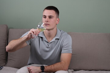 portrait of a young white male sitting on a couch and drinking a glass of white wine