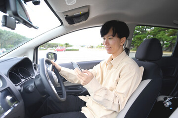 スマホ通話をしながら車を運転する若いアジア人男性
