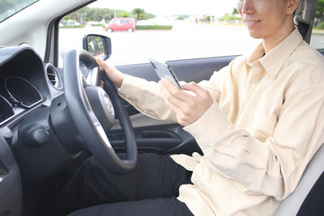 スマホ通話をしながら車を運転する若いアジア人男性