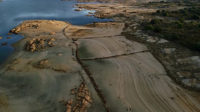 Aerial drone flying over rocky lakeside terrain with visible stone structures and lake water in Spain