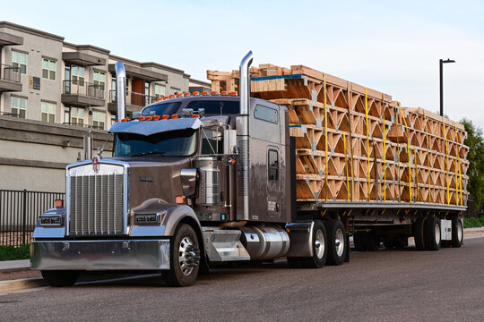 Semi-truck hauling a flatbed trailer loaded with stacked wooden trusses, representing construction logistics, building materials transport, freight distribution, and commercial supply chain operations