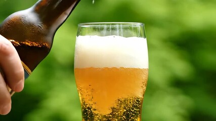 Refreshing golden beer is expertly poured from a classic brown bottle into a tall clear glass creating a perfect frothy head against a vibrant blurred green outdoor background evoking a sense of rela.