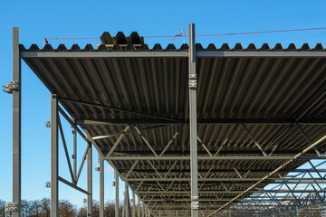Obraz premium Steel warehouse roof construction with metal trusses and corrugated sheets against clear blue sky