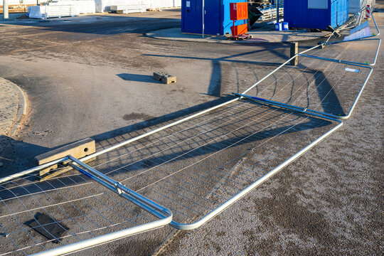 Wind-blown temporary construction site fence knocked down on asphalt near blue site containers