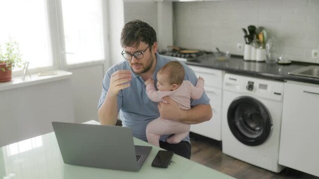 Stressed dad multitasking with infant and laptop in modern kitchen