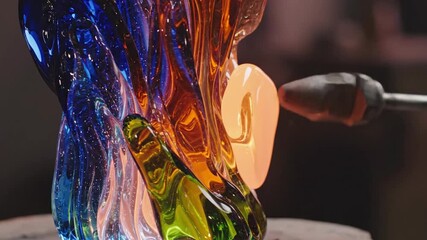 Artist shaping molten glass sculpture with vibrant colors and internal light