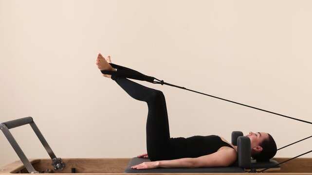 Woman performing pilates exercise on reformer machine using stretch bands 