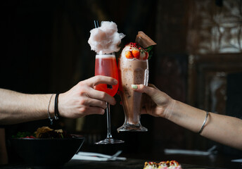 Two people are holding up their drinks, one of which is a strawberry milkshake
