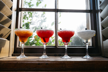 Four martinis are lined up on a table next to a window