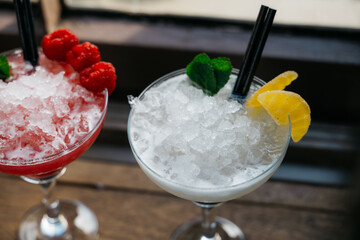 Two drinks with straws in them, one is a pink drink with raspberries