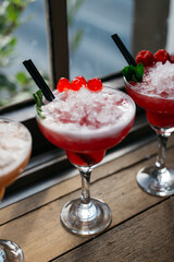 Three martinis with raspberries on top are sitting on a wooden table