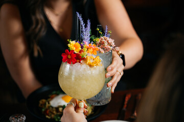 A woman is holding a glass of a drink with flowers in it