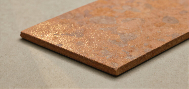 A close-up of a rectangular tile with a copper-colored, textured surface featuring speckled patterns and a metallic sheen. - Powered by Adobe