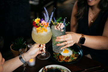Two women are holding up their drinks and toasting to each other