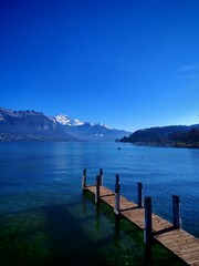 Obraz premium Wooden pier or dock on the Annecy lake. Snow-capped mountains Mont Baret in the background