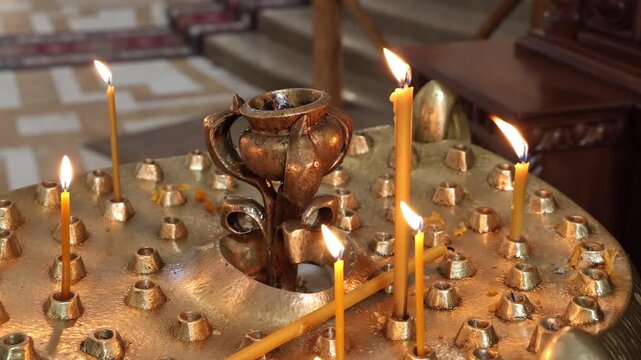 Thin wax candles burning in a golden candelabrum inside a church. A religious atmosphere for prayer, faith, and memorial ceremonies