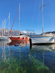 Fototapeta premium Sailing boats and yachts are at the harbour of Annecy lake. Snow-capped mountains Mont Baret in the background