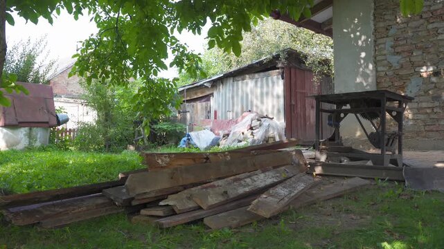 Old yard with piles of boards and metal circular saw, Village yard with pile of old wooden boards and old metal circular saw