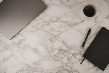 A clean workspace features a laptop, a cup of coffee, and a notebook on a marble surface. This setting offers ample negative space for text and inspiration, perfect for work or study