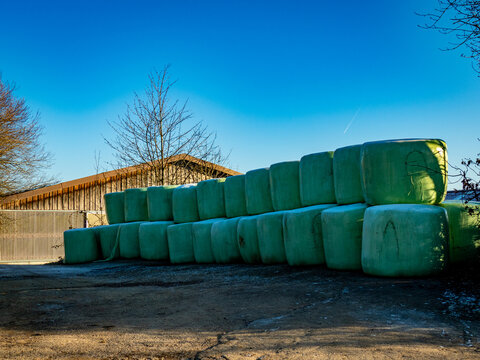 Silageballen lagern vor einer Scheune