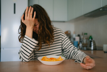 Woman with discomfort holding her forehead, feeling unwell with a headache and nausea, sitting at a...