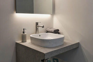 Fototapeta premium Modern white ceramic sink on concrete countertop with chrome faucet and soap dispenser in bathroom corner