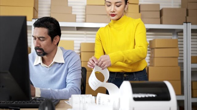 Business owner and employee labeling packages using printer and tablet in warehouse office