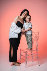 Woman and young boy sharing a joyful moment in a bright studio with pink background, showcasing love and connection during their playful interaction