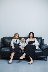 Family bonds shine brightly as mother and children relax on a cozy black couch in a modern living space during a calm afternoon