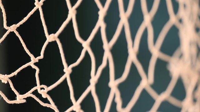 Close up of durable white fabric fishing net tied with knots for strength displayed on turquoise, dark blue, and black background highlighting texture and craftsmanship of netting