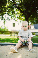 Young child plays with a toy truck in a sunny park sandbox surrounded by greenery, enjoying a playful afternoon in the warmth of summer