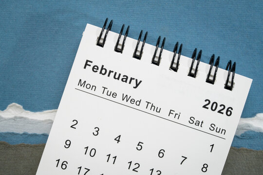 February 2026 - small spiral desktop calendar against art paper abstract, time and business concept