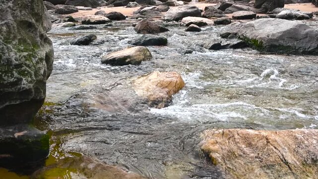 Clear water stream flows over smooth rocks toward the sandy Atlantic shore at Praia das Ma&ccedil;&atilde;s, creating relaxing natural motion